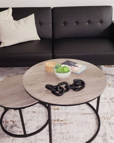 Bright living room with black sectional sofa, round coffee table, TV stand, and olive tree