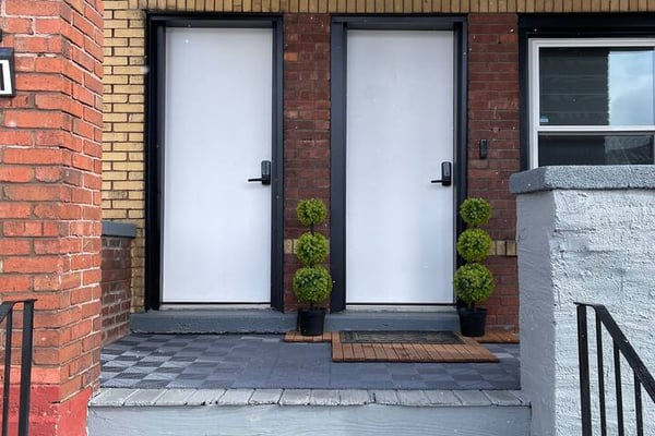 Brick patio with two white doors, potted topiaries, and metal railings leading to entrance