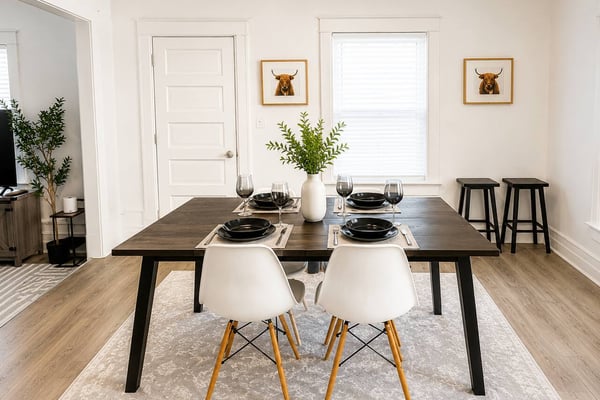 Dining room with dark wood table, white chairs, place settings, white doors, framed bull artwork, and window with natural light
